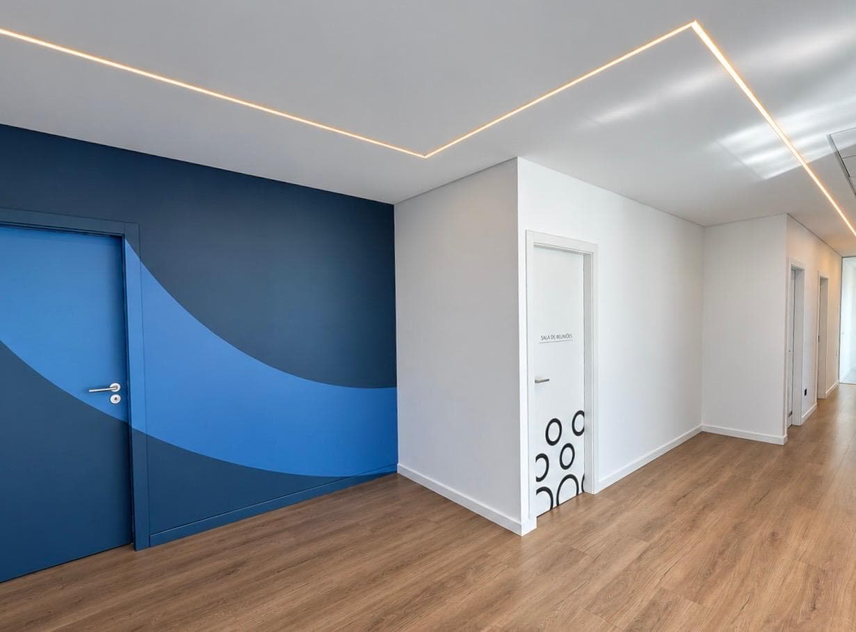 Corredor com parede azul de onda, porta da sala de reuniões e perfil de luz LED embutido no teto